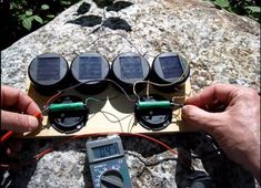 two hands are working on an electronic device that is sitting on top of a rock