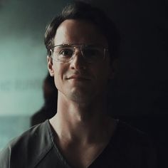 a man wearing glasses standing in a dark room