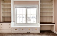 an empty room with built in bookshelves and drawers on either side of the window