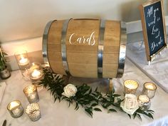 a wooden barrel sitting on top of a white table covered in candles and greenery