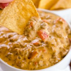 a hand holding a tortilla chip and dipping it into a white bowl filled with salsa