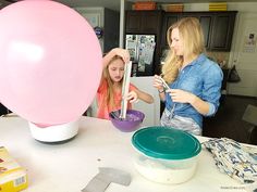 two women in the kitchen preparing food with balloons on the table behind them, and one woman holding a measuring spoon