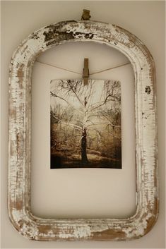 an old white frame hanging on a wall with a tree in the middle and some clothes pins attached to it