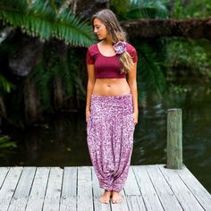 a woman standing on a dock wearing a purple skirt and crop top with flowers in her hair