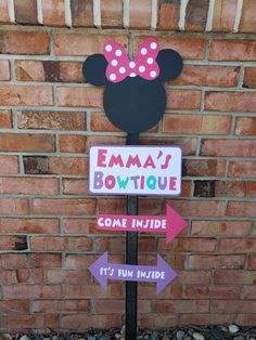 a sign with minnie mouse on it in front of a brick wall