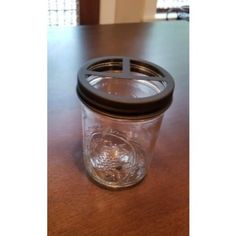 a glass jar with a black lid sitting on top of a wooden table next to a window