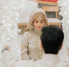 a bride looking at her groom in front of an archway with white flowers on it