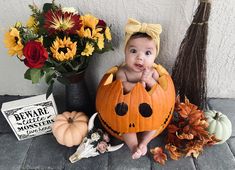 a baby sitting in a pumpkin costume next to some flowers and other halloween decorations on the ground