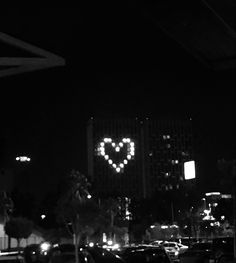 cars parked on the street in front of buildings at night with heart shaped lights above them