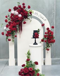 red flowers and greenery decorate the top of a white pedestal