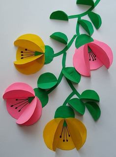 paper flowers are arranged on a white surface with green leaves and yellow petals in the center