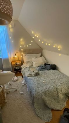 an unmade bed sitting in a bedroom next to a window with fairy lights on it