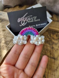 a hand holding a rainbow ring in front of a box with a card on it