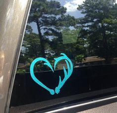 a heart shaped sticker sitting on the side of a car window with trees in the background