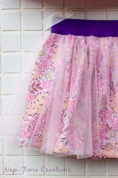 a pink and purple flowered dress hanging on a white brick wall with the words nap time creations