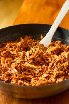 a skillet filled with pulled pork on top of a wooden table next to a spoon