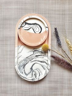 a marble plate with an abstract design on it next to some dried flowers and plants