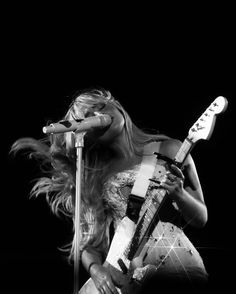 a woman holding a guitar and singing into a microphone