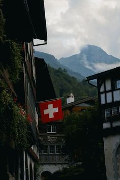 a swiss flag is hanging on the side of an old building with mountains in the background