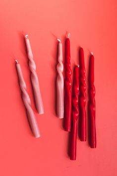 four candles are lined up on a pink surface, one is white and the other is red