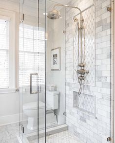 a white bathroom with glass shower doors and marble tile flooring, along with a walk in shower