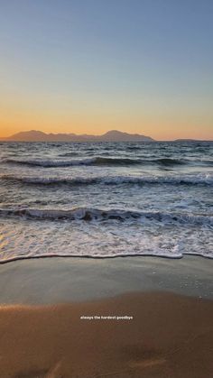 the sun is setting over the ocean with waves coming in to shore and mountains in the distance