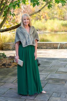 a woman in a long green dress and fur stoler standing on a brick walkway