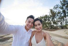 a man and woman taking a selfie on the beach with trees in the background