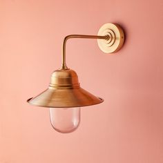 an old fashioned brass wall light on a pink wall with a clear glass bulb hanging from the side