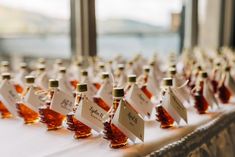 there are many small bottles with labels on them sitting on a long table in front of a window