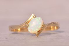 The Gama: Natural Australian Opal Bypass Ring in Yellow Gold. This exquisite ring features a central oval cabochon natural Australian opal, set at an angle in the center. The design is elegantly completed with a tapered bypass-style shank that gracefully hugs the centerpiece. Crafted in 14-karat yellow gold, the ring is currently sized at 6 but can be adjusted to fit any finger size for an additional fee upon request. Love this piece, but don't have the money to spend right now? We offer FREE la Elegant Oval Opal Ring With Polished Finish, Formal Oval Cabochon Opal Ring, Polished Opal Ring In Oval Cabochon Shape, Opal Oval Cabochon Ring With Polished Finish, Polished Opal Oval Cabochon Ring, Elegant Ethiopian Opal Ring For Anniversary, Elegant Opal Cabochon Ring, Elegant Ethiopian Opal Cabochon Rings, Elegant Opal Oval Cabochon Ring Gift