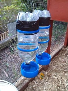 three water bottles are attached to the side of a chicken coop with plastic cups on them