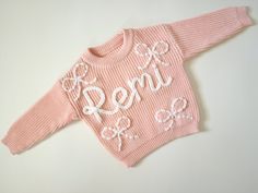 Made to order hand embroidered bow sweaters perfect for your newborn baby girl, toddler birthday present or baby shower gift!  All names will be written in cursive unless you specify otherwise. These are handwritten, no two sweaters will look the same!  For reference, the "Remi" sweater pictured is baby pink with extra chunky WHITE yarn. White yarn is not listed in my yarn colors currently, but is available in extra chunky or thin.  PERSONALIZATION Please include the color of sweater, name/word Hand Embroidered Sweater, Embroidered Sweaters, Embroidery Yarn, Sweater Designs, Embroidered Bow, Baby Girl Toddler, Kids Jumpers, Toddler Sweater, Bow Sweater