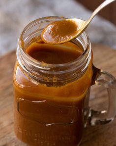 a spoon full of caramel sauce sitting on top of a wooden table next to a jar