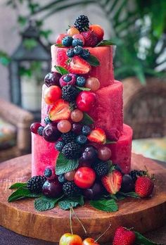 a watermelon cake with berries and cherries on the top is sitting on a wooden platter