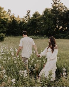 a man and woman holding hands while walking through tall grass