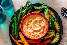 a black plate topped with asparagus and carrots next to a bowl of hummus