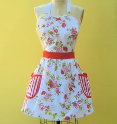 a dress on a mannequin with flowers and red ribbon around the waist, in front of a yellow background