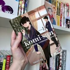 a person holding up a book in front of bookshelves with anime characters on them