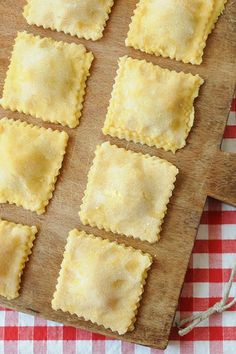 some ravioli on a wooden cutting board next to a red and white checkered tablecloth