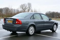 a grey car parked in a parking lot on a rainy day with trees in the background