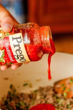 a person pouring ketchup into a bowl of food