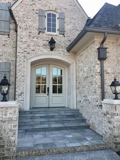 the front entrance to a house with two lamps on each side and stone steps leading up to it