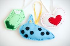 three felt ornaments hanging from strings on a white surface with a red heart in the middle