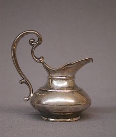 an antique silver pitcher on a gray background with swirly handles and curved handle is shown