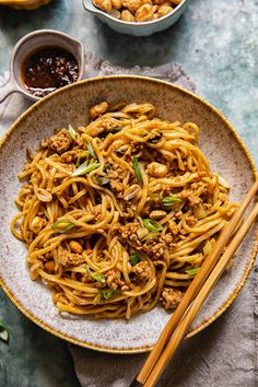 a plate full of noodles and meat with chopsticks next to bowls of sauce