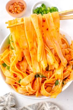 a white bowl filled with noodles and carrots on top of a table next to chopsticks