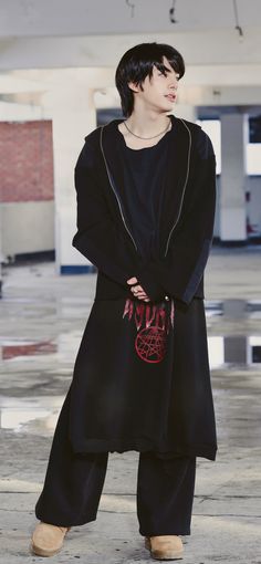 a man standing in an empty parking lot wearing a black coat with red letters on it