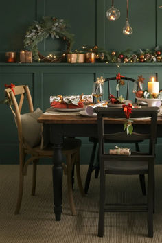 a dining room table set for christmas dinner with candles and greenery on the wall