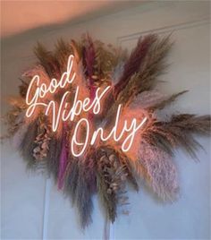 a neon sign that says good vibes only on top of some feathers and pine cones